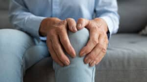 Closeup of older woman's hands around her knee, experiencing joint pain in the winter